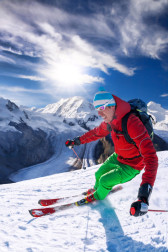 Skier skiing downhill in high mountains against blue sky