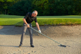 senior-golfer-rake-the-the-sand-in-a-bunker